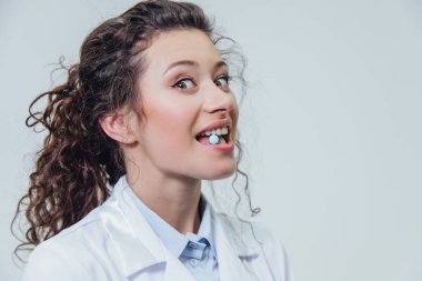 Beyaz bir sabahlık genç doktor doktor gri bir arka plan üzerinde duruyor. Bu sırada o güvercin güvercin tutar. Bu sırada, o ona bir işaret parmağı gösterir.