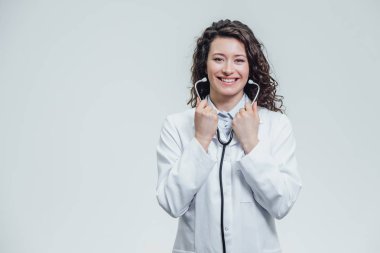 Sana bakmak ve phonendoscope elini tutan bir ciddi genç kadın beyaz bir kadın bir laboratuvar elbise içinde. Bir çok siyah saçlı kadın - beyaz üniforma giyen bir doktor portresi. ,