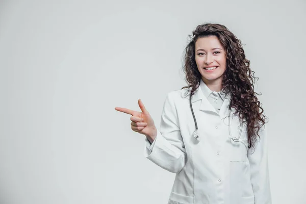 Молода жінка-лікар у білому одязі. Вказівка на індексний палець чудова ідея. На сірому тлі . — стокове фото