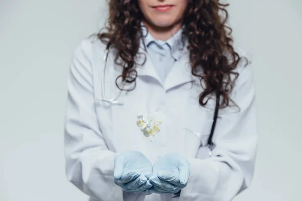 Um jovem médico bonito vestido com um roupão branco e luvas azuis. Durante este tempo, ele está em um fundo cinza e coloca os comprimidos no close-up . — Fotografia de Stock