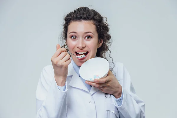 Die Ärztin im weißen Morgenmantel hat einen grauen Hintergrund. Mädchen sind drogenabhängig. Er will Medizin vom Teller essen. — Stockfoto