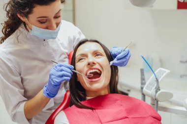 Genç bir kadın doktor bir maske ve Tıbbi eldivenler giymiş. Bu sırada hastanın tıbbi bir ayna ve bir yoklama alır.