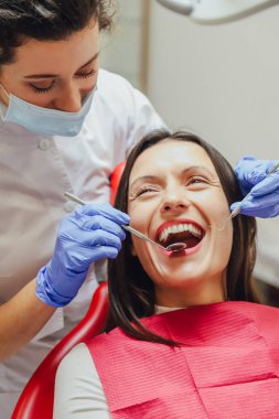 Genç bir kadın doktor bir maske ve Tıbbi eldivenler giymiş. Bu sırada hastanın tıbbi bir ayna ve bir yoklama alır.
