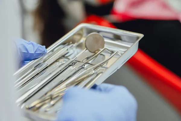 Instrumenty stomatologiczne są wyświetlane w rękach lekarza stomatologa. Ubrany w niebieski rękawice. W srebrnej tacy medycznych w biurze Dentyści. — Zdjęcie stockowe