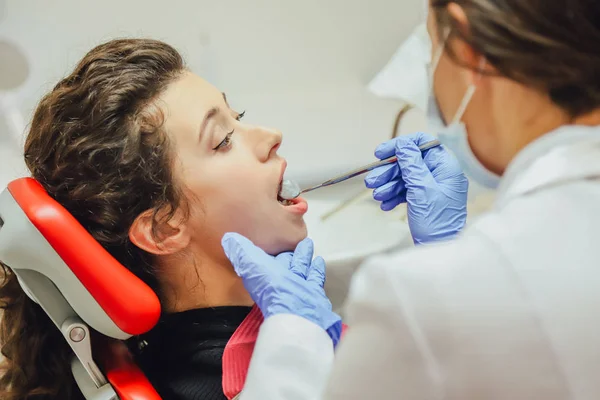 Doktor dělá profesionálně. Usmívající se krásná dívka s bílými zuby, zkoumal zubní lékař na klinice. Lékař je dobrá žena pracující v masku a rukavice. — Stock fotografie