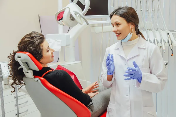 A női fogorvos beszél a beteg. Fogorvos szállítására a modell a kezében. Során az orvos kesztyű maszkot visel. — Stock Fotó