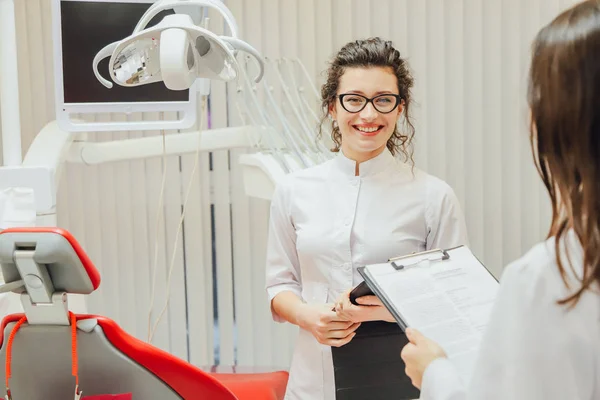 Portret uśmiechający się dentysty i asystent, patrząc na Schowka w nowoczesnej kliniki stomatologiczne. Ubrany w medyczne białe szlafroki. — Zdjęcie stockowe