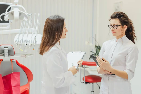 Two doctor dentist in the office. Beautiful young women. Stand and talk dressed in medical white clothes. — Stock Photo, Image