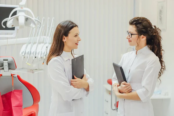 Dwa lekarz dentysta w biurze. Pięknych młodych kobiet. Stoją i talk medyczny ubrany w białe szaty. — Zdjęcie stockowe