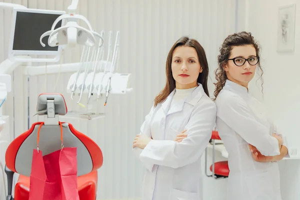 Twee arts-tandarts in het kantoor. Mooie jonge vrouwen. Permanent met een vleugje van elkaar. Als we kijken naar de camera. Gekleed in medische witte kleren. — Stockfoto