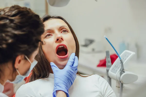 Jeune femme assise sur une chaise dentaire pour rendez-vous chez le médecin. Pendant ce temps, elle était très inquiète de la peur, a ouvert ses grands yeux. Un médecin est une bonne femme en vêtements médicaux, ce qui rend un — Photo