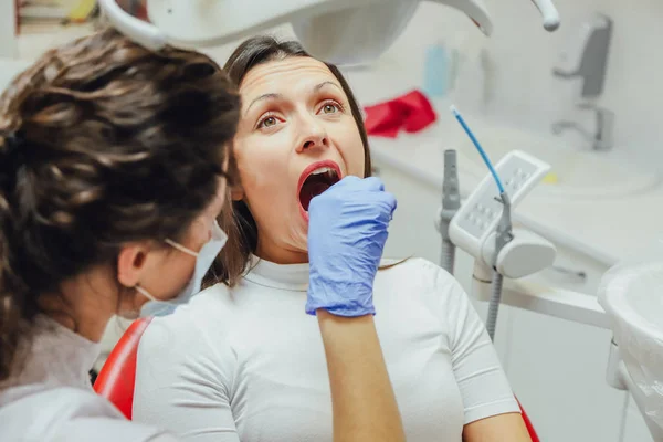 Młoda kobieta siedzi w Fotel dentystyczny dla powołania lekarza. W tym czasie była bardzo martwi się o strachu, otworzyła duże oczy. Lekarz jest dobrą kobietą w ubrania medyczne, co sprawia, że — Zdjęcie stockowe