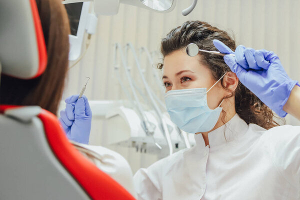 A young wife sits in a dental chair at a doctors appointment. During this time, she was very alarmed by fear, opened the roses with big eyes.