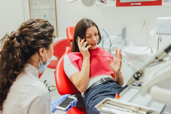 Młoda kobieta siedzi w Fotel dentystyczny dla powołania lekarza. W tym czasie była bardzo martwi się o strachu, otworzyła duże oczy. Lekarz jest dobrą kobietą w ubrania medyczne, co sprawia, że — Zdjęcie stockowe