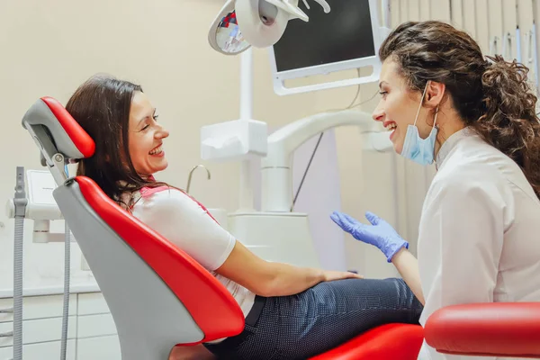 A beteg az a fiatal nő a fogorvosok kinevezését. Ez idő alatt a fogorvosi székben ül, és beszél, hogy egy orvos. Orvos egy pozitív fiatal gyönyörű nő. — Stock Fotó