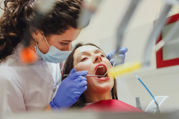 Mladá lékařka je oblečená v masku a lékařské rukavice. Během tohoto pacient obdrží lékařské zrcátko a sondy. Mladý pacient je zvažován zubního lékaře v zubní praxi — Stock fotografie