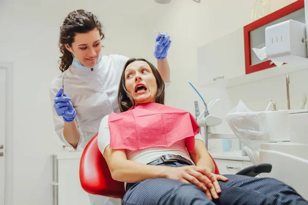 Een jonge vrouw is geschokt door de angst voor tandheelkundige instrumenten die ze naar haar kijkt, wijdopen ogen. Het begrip angst voor een tandarts en tandheelkundige behandeling. — Stockfoto