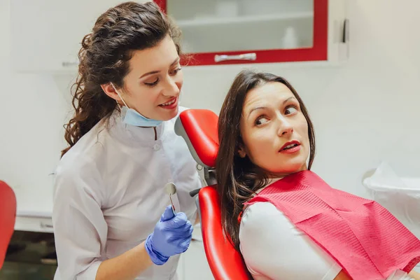 Een jonge vrouw is geschokt door de angst voor tandheelkundige instrumenten die ze naar haar kijkt, wijdopen ogen. Het begrip angst voor een tandarts en tandheelkundige behandeling. — Stockfoto