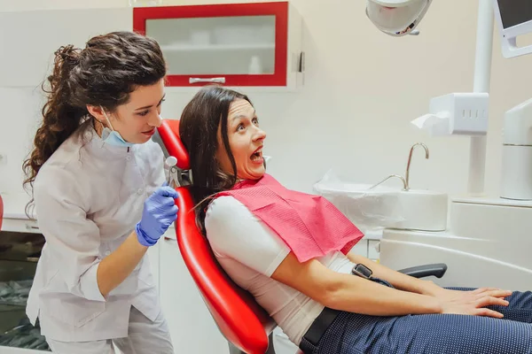 A young woman is shocked by the fear of dental instruments that she looks at her, wide-open eyes. The notion of fear of a dentist and dental treatment. — Stock Photo, Image