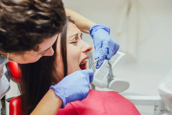 Een jonge vrouw is geschokt door de angst voor tandheelkundige instrumenten die ze naar haar kijkt, wijdopen ogen. Het begrip angst voor een tandarts en tandheelkundige behandeling. — Stockfoto