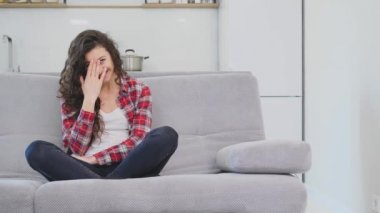 Güzel bir kadın TV izliyor ve kanepede oturuyor ve elinde uzaktan kumandayı tutuyor.