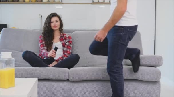 Hermosa chica y un joven sentado en el sofá y ver la televisión. La gente se relaja en el sillón.Joven con gafas y camisa azul . — Vídeos de Stock