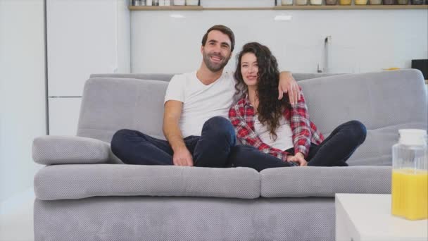 Beautiful girl and a young man sitting on the couch and watch TV. People relax on the couch.Young man in glasses and blue shirt. — Stock Video