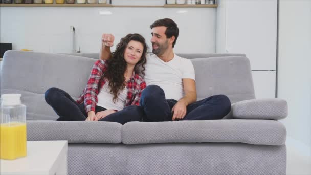 Menina bonita e um jovem sentado no sofá e assistir TV. As pessoas relaxam no sofá. Jovem de óculos e camisa azul . — Vídeo de Stock