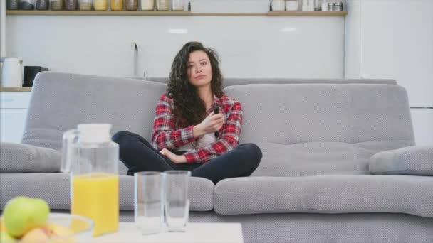 Krásná dívka a mladý muž sedí na gauči a sledují televizi. Lidé odpočívejte na gauči. Mladý muž s brýlemi a modrou košilí. — Stock video