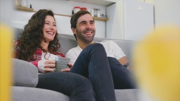 Pareja joven relajándose en su apartamento, tumbada en el sofá y viendo la película . — Vídeo de stock