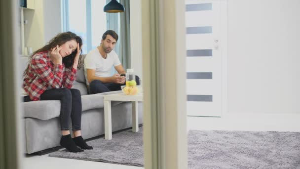 Ein nachdenkliches, nachdenkliches junges Mädchen, das über die Beziehungsprobleme nachdenkt. mit einem beleidigten Jungen auf der Couch sitzen. — Stockvideo