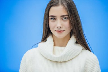 Genç iş kız beyaz sıcak Kazak giymiş. Bu süre içinde bu mavi bir arka plan üzerinde duruyor. Uzun, güzel saçlı.