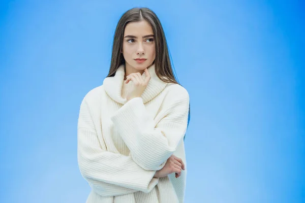 Imagen de la joven feliz de pie sobre un fondo azul. Mira a la cámara. Durante este tiempo ella está vestida con un suéter blanco cálido . —  Fotos de Stock