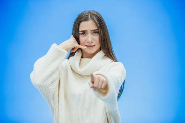 Красивая молодая девушка на синем фоне. Девушка показывает телефонный звонок с жестом. Одетый в белый теплый свитер. Имеет длинные черные волосы . — стоковое фото