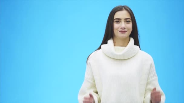 Ritratto di una giovane ragazza. Ragazza alta su sfondo blu. Durante questo periodo è vestita con un maglione bianco caldo. Mostra la classe gestuale con le mani . — Video Stock