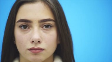 Güzel genç kız mavi bir arka plan üzerinde ayakta. Bu süre içinde o beyaz bir Kazak giymiş. Uzun siyah saçlı.
