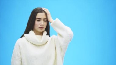 Genç iyi iş kız mavi bir arka plan üzerinde ayakta. Sırasında bu sürpriz, o elini kafasına, bir şeyler hatırlamaya koyar.