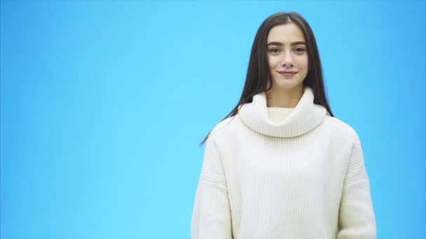 Retrato de um negócio de raparigas. Menina alta em um fundo azul. Durante este tempo, ela está vestida com uma camisola branca quente. Mostra a aula de gestos com as mãos . — Vídeo de Stock