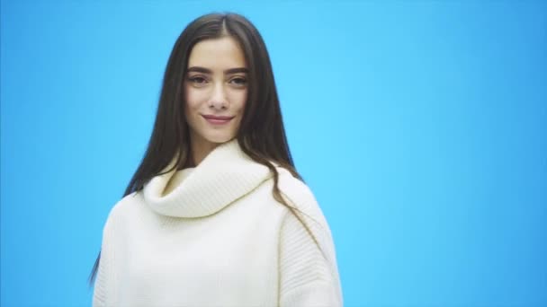 Young energetic girl stands on a blue background. During this smiles, having adjusted hair. — Stock Video