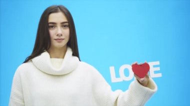 Genç güzel kız beyaz elbise giymiş. Bu süre içinde bu mavi bir arka plan üzerinde duruyor. Bir kelime aşk elinde tutan.