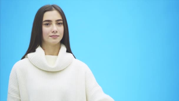 Joven chica bonita vestida con ropa blanca. Durante este tiempo se encuentra sobre un fondo azul. Tiene una palabra de amor en las manos . — Vídeos de Stock