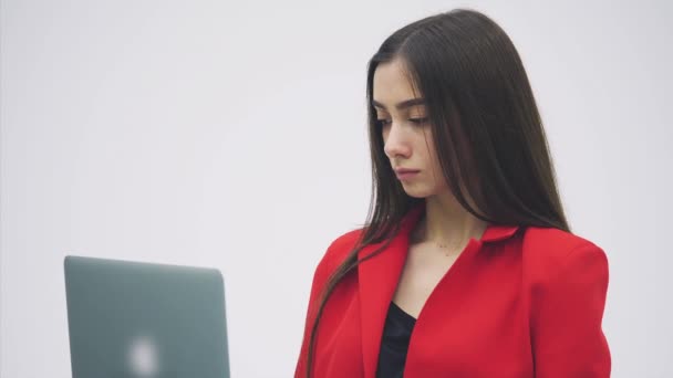 Das Bild einer jungen Geschäftsfrau. isoliert auf einem grauen Hintergrund. Es lohnt sich, einen grauen Laptop zu benutzen. bekleidet mit einer roten Jacke. — Stockvideo