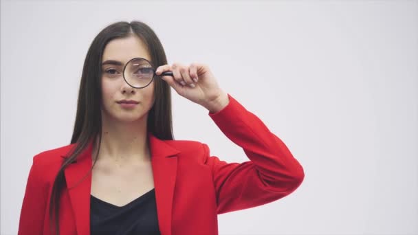 Expresiones graciosas. Una mujer conmocionada mirando lupa. Una chica sorprendida mira a abrir las llaves con grandes ojos a través de una lupa, aislada sobre un fondo blanco . — Vídeo de stock