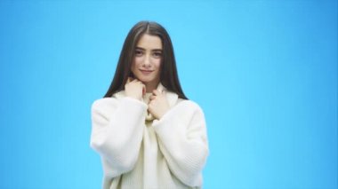 Güzel genç mavi bir arka plan üzerinde duran kız. Bu süre içinde o beyaz bir sıcak Kazak giymiş. Kameraya bakarak gülümsüyordu. Yavaş video.