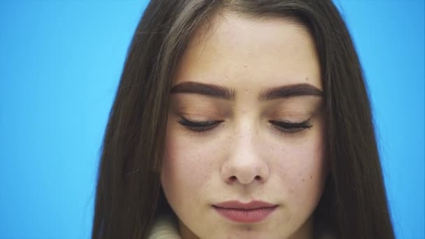 Young pretty girl standing on a blue background. During this time she is dressed in a white warm sweater. Looking at the camera. — Stock Video