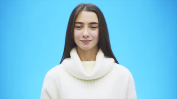 Portrét šťastné mladé ženy na sobě bílý Teplý svetr. Během tohoto času, gesto rukou srdce pořadů a miluje. Izolované na modrém pozadí. — Stock video