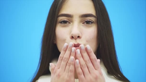 Young beautiful brunette woman on an isolated background. Showing an air kiss with his hands and mouth. Smiling confidently and happily. On a blue background. — Stock Video