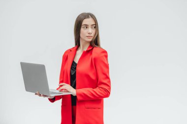 Genç iş kadını görüntüsü. Gri bir arka plan üzerinde izole. Gri bir dizüstü bilgisayar kullanarak buna değer değil. Kırmızı bir ceket giymiş.