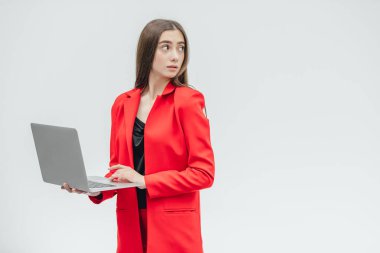 Genç iş kadını görüntüsü. Gri bir arka plan üzerinde izole. Gri bir dizüstü bilgisayar kullanarak buna değer değil. Kırmızı bir ceket giymiş.