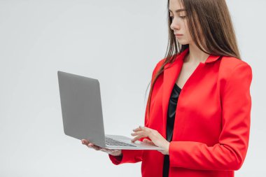 Genç iş kadını görüntüsü. Gri bir arka plan üzerinde izole. Gri bir dizüstü bilgisayar kullanarak buna değer değil. Kırmızı bir ceket giymiş.